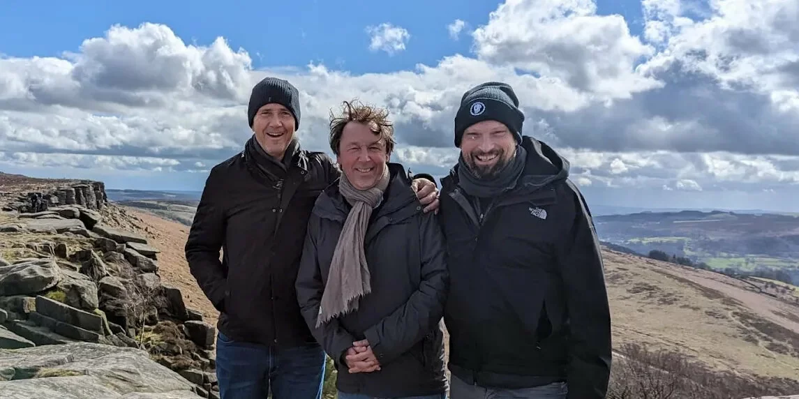 a group of three male friends posing for a picture in front of a cliffy landscape