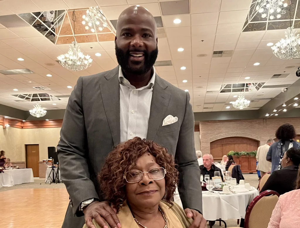 Fredrick Riley standing behind his mother at an event.