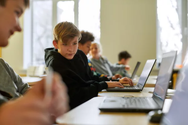 Portrait of caucasian schoolboy looking at the laptop of his neighbor while sitting in a classroom with other pupils during a lesson in modern smart school. STEM disciplines. Selective focus 2026/02/AdobeStock_336301921_1-e1770939934225.jpeg 