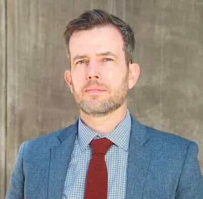 A professional headshot of Chris Grove in business attire.