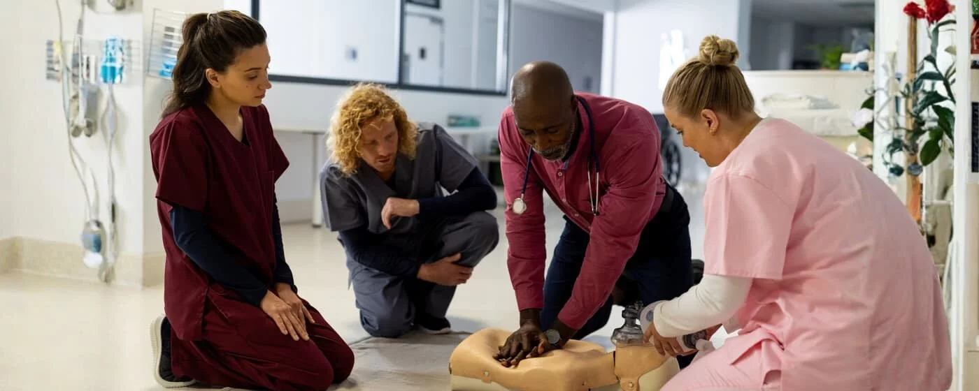Two men and two women in nursing scrubs doing CPR vocational training on a training dummy