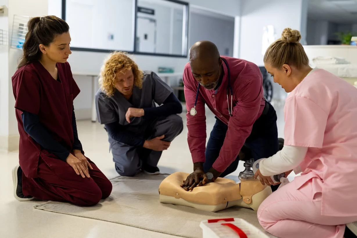 Two men and two women in nursing scrubs doing CPR vocational training on a training dummy