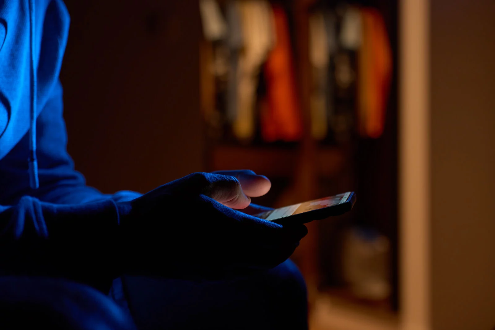 Close-up of male hands holding smartphone with glowing screen in dark room. Man using smartphone at night. Concept of technology and online communication