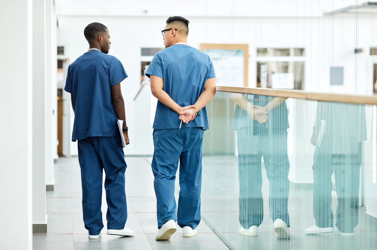 Back view full length of two doctors wearing blue uniform walking in hall of modern clinic