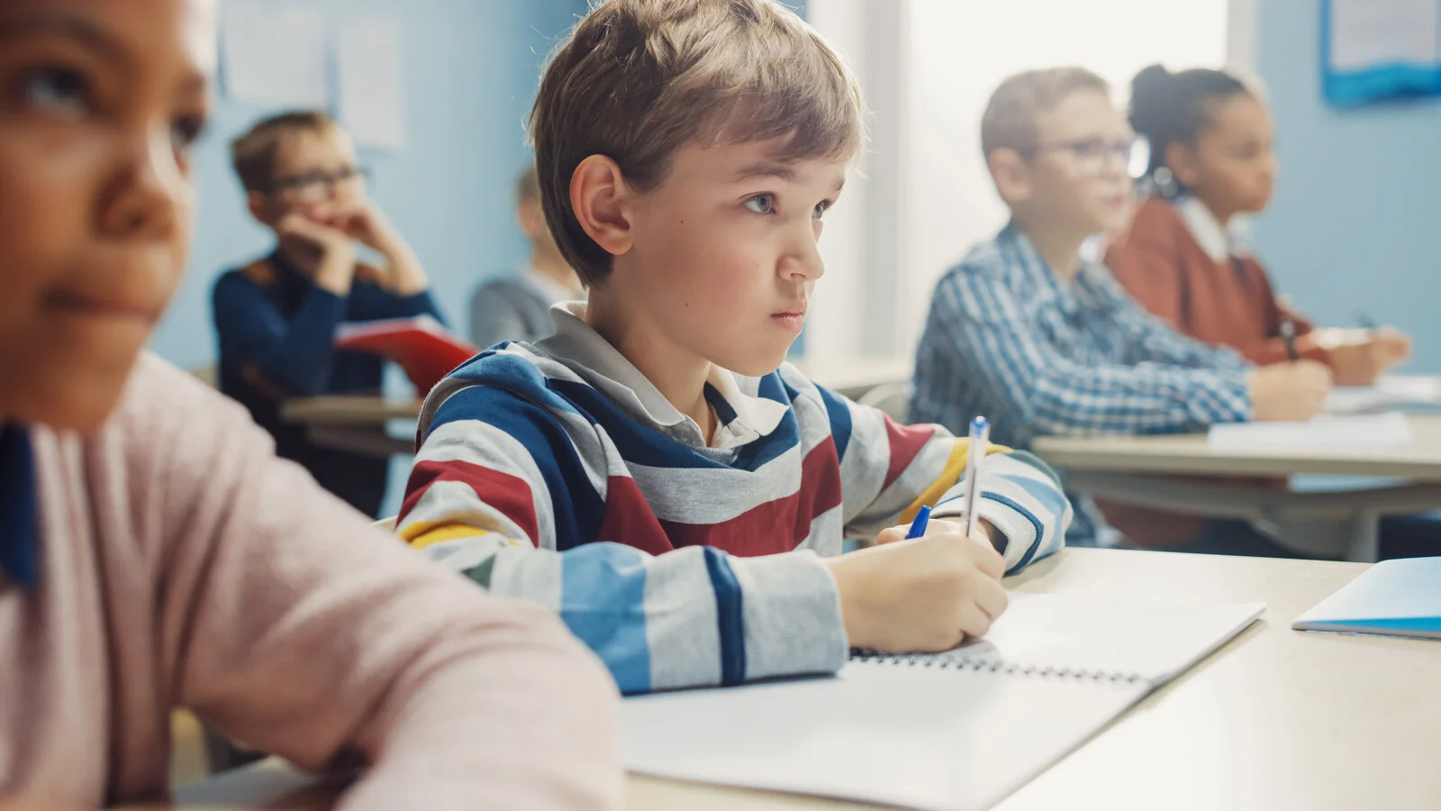 In Elementary School Class: Portrait of Brilliant Caucasian Boy Writes in Exercise Notebook, Taking Test and Writing Exam. Diverse Group of Bright Children Working Diligently and Learning 2026/05/AdobeStock_361379517.jpeg 