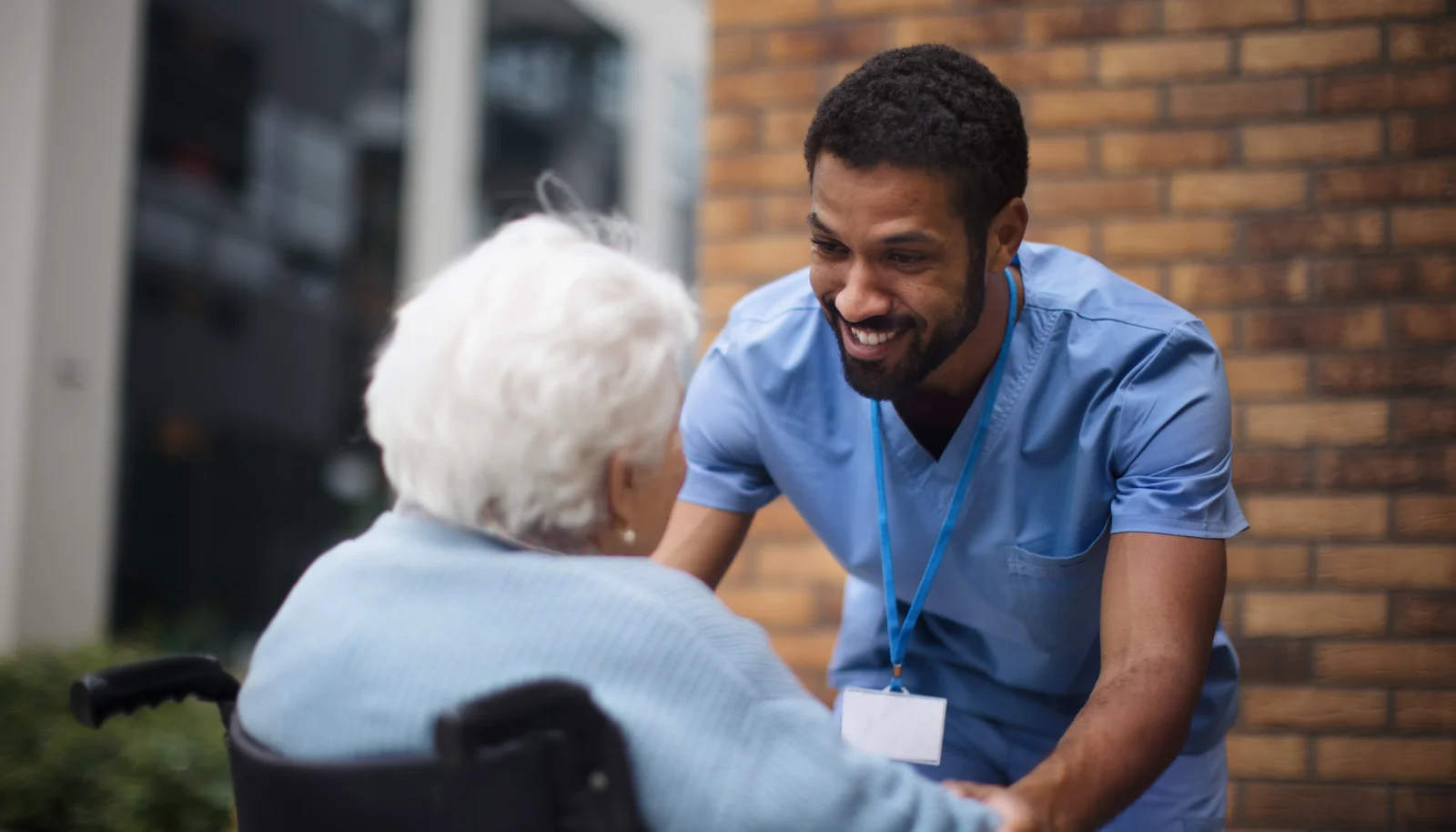 Male medical professional talks with elderly patient in wheelchair