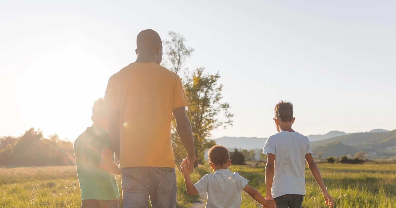 Father and kids walking together at sunset in a green field