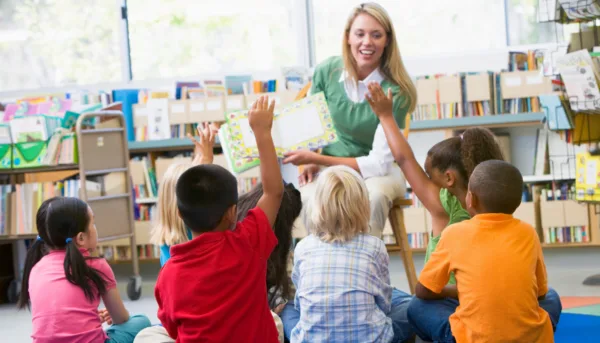Students raise hands as a teacher reads to them in a school classroom Students raise hands as a teacher reads to them in a school classroom