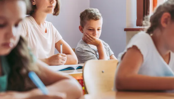 Boy rests head against palm in classroom
