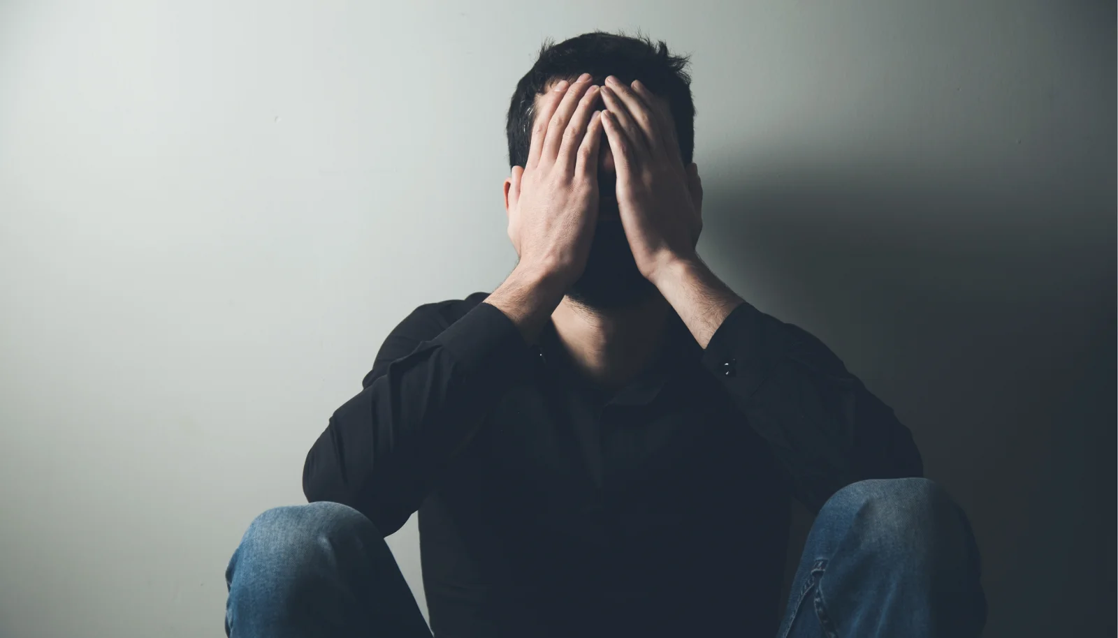 Man sitting on the floor with his hands covering his face
